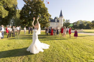 la jolie mariée dans sa belle robe blanche de noce lance son bouquet de mariage aux demoiselles sur la pelouse du parc du Chateau Agassac à Ludon-Médoc