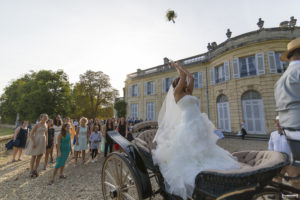 Dans le parc du Chateau de la Dame Blanche au Taillan Medoc, la jolie mariée dans sa belle robe blanche lance son bouquet de mariage aux demoiselles depuis la calèche qui l'a conduite au lieu de la réception et du vin d'honneur du mariage