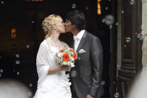 couple de jeunes maries indien et francaise qui s'embrassent à la sortie de l'église sous les bulles et les applaudissements des témoins et de la famille