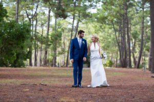 couple de jeunes mariés marchant main dans la main dans le sous bois de la forêt médocaine au bord du lac de carcans maubuisson en Gironde sous l'oeil du photographe de mariage à Bordeaux Sébastien Huruguen