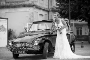 magnifique mariée posant en robe blanche bouquet de fleurs à la maison devant la citroen dyane qui l'a amené a la cérémonie de son mariage au bord des vignes de la rive droite en Gironde sous l'oeil du photographe de mariage à Bordeaux Sébastien Huruguen