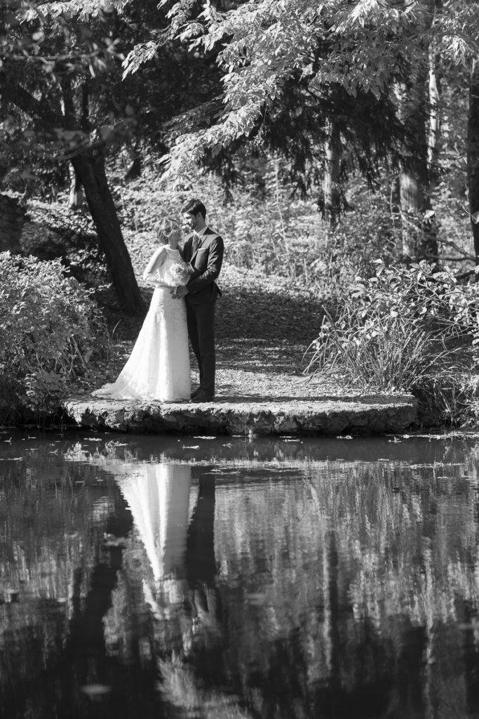 couple de jeune mariés au bord d'un plan d'eau en noir et blanc avec un joli reflet
