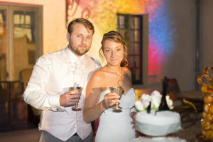 Couple de jeunes mariés qui trinquent lors de la présentation du dessert au repas de mariage après avoir couper le gateau, présentation du gateau en extérieur, robe de mariée, sebastien huruguen photographe mariage bordeaux