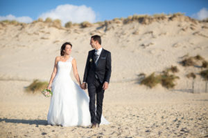 Couple de mariés marchant main dans la main sur le sable de la plage de Carcans Maubuisson dans le Médoc en Gironde sous l'oeil du photographe de mariage à Bordeaux Sébastien Huruguen