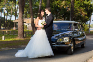 jeunes mariés dans la lumière devant la voiture de leur mariage en Gironde sous l'oeil du photographe de mariage à Bordeaux Sébastien Huruguen