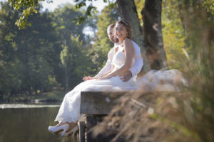 Jolie mariée et son mari en train de sourire assis au bord d'un plan d'eau du parc de majolan à Blanquefort avec de jolis escarpins à hauts talons blancs avec plateforme photographe mariage bordeaux sebastien huruguen