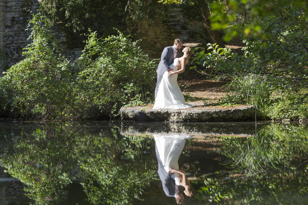 Couple de jeunes mariés posant au bord d'un lac avec un joli reflet dans l'eau, photo prise lors d'une seance trash the dress au parc de majolan a blanquefort dans la région bordelaise par le photographe de mariage sebastien huruguen à Bordeaux