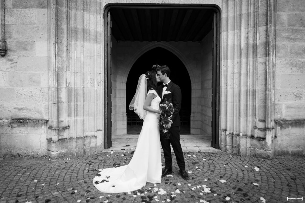 belle photo en noir et blanc où le couple de jeunes mariés s'embrassent à la sortie de la messe à Macau