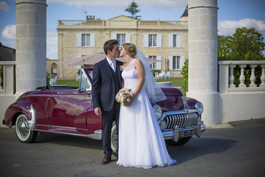 Photographe Mariage Bordeaux Sebastien Huruguen chateau lafitte laguens yvrac couple de maries qui s'embrassent devant entree du chateau et vieille voiture peugeot