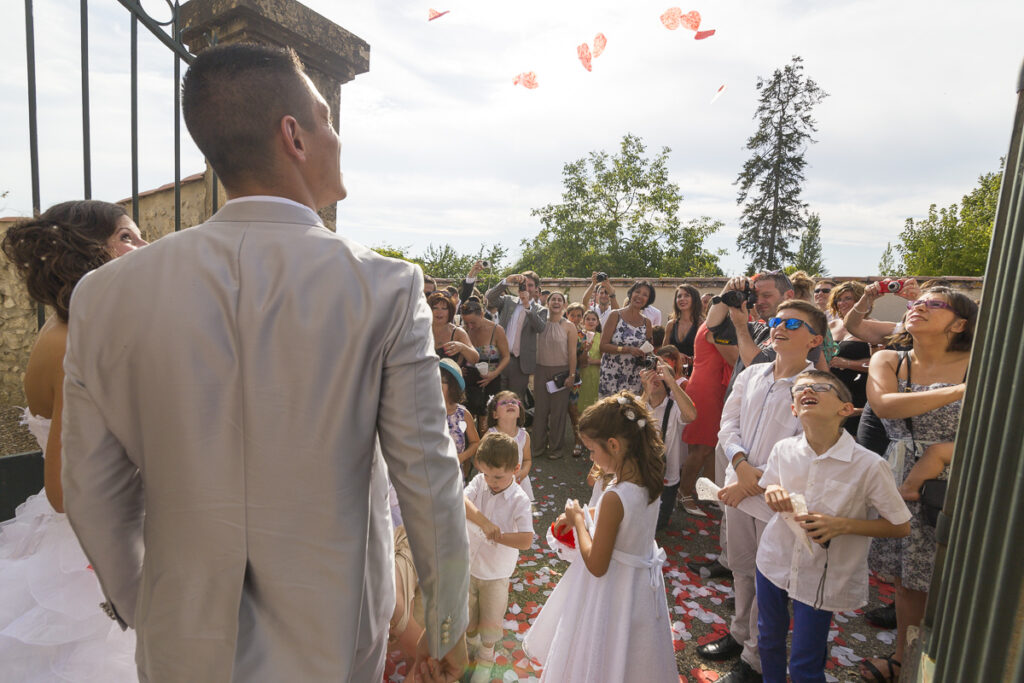 sortie d'un couple de maries de l'eglise notre dame de beyssac a marmande avec des coeurs qui volent dans le ciel devant les invités et témoins sebastien huruguen