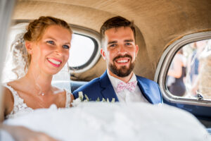 Nouveaux mariés souriants assis à l'arrière d'une Renault 4CV de 1955 lors de leur mariage au Château Larrivet Haut-Brion.