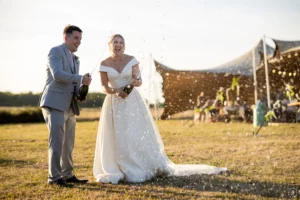 Mariés F&T faisant sauter le champagne avec joie devant leur tente nomade lors d'un mariage champêtre en Deux-Sèvres